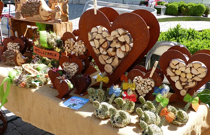 Marktstand mit Holzherzen, Holztieren und dekorativen Figuren aus Stroh auf einem mit Leinen bedeckten Tisch.