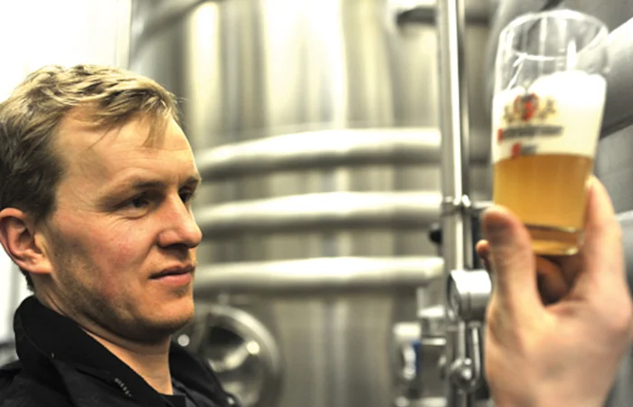 Der Braumeister hält ein Glas mit frisch gebrauten Bier in der rechten Hand und begutachtet es.