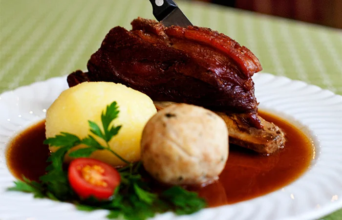 Teller mit Schweinebraten, Knödeln, Soße, Petersilie und Tomatenscheibe auf grün kariertem Tischdecke im Gasthof Weisses Lamm in Kelheim.