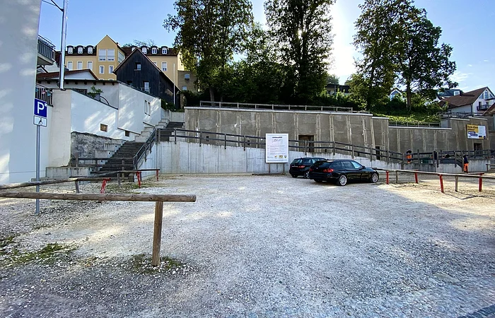 Parkplatz mit zwei schwarzen Autos, Treppen und Bäumen im Hintergrund bei sonnigem Himmel