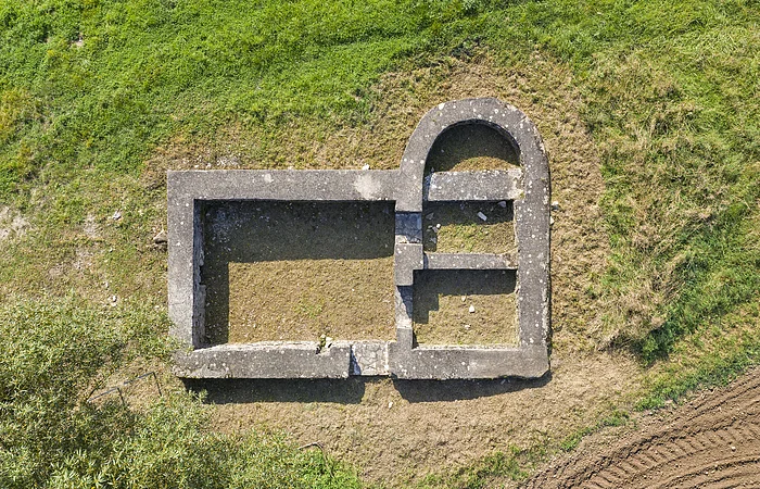 Luftaufnahme von rechteckigen und halbrunden Steinmauern einer Ruine auf Grasboden.