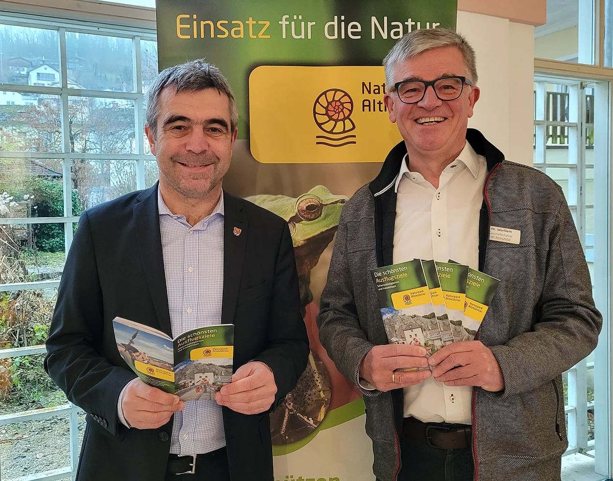 Neue Broschüre „Die schönsten Ausflugsziele“ Zwei Männer stehen vor einem Banner mit der Aufschrift „Einsatz für die Natur“ und halten Broschüren vom Naturpark Altmühltal.