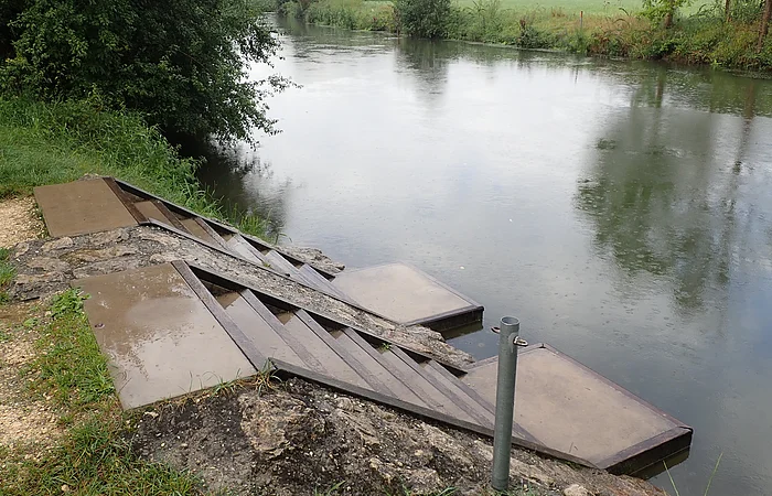 Ufer mit Treppe und Plattformen am ruhigen Fluss bei bewölktem Himmel und Regen.
