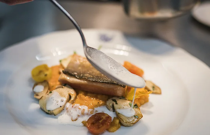 Auf weißem Teller wird vom Koch Regelmannsbrunner Bachsaibling mit Steinpilzen und Risotto vom Muskatkürbis (aus dem Urdonautal)angerichtet angerichtet. "Zum Klosterbräu" in Bergen im Naturpark Altmühltal
