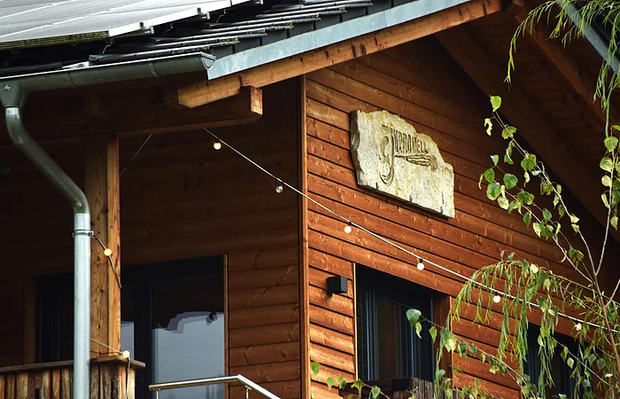 Holzhaus mit Solarzellen auf dem Dach, Lichterkette und Steinplatte mit Schrift an der Fassade
