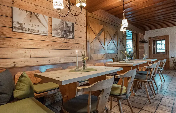 Modern gestalteter Teil der Gaststube in der Krone in Kinding. Verwendung von Holz vereint Tradition und Moderne zum Beispiel durch helle, naturbelassene Holzwände, einer Holzdecke, eine Schiebetüre im Scheunenstil sowie helle Sitzmöglichkeiten mit Sitzkissen in gedeckten Farben.