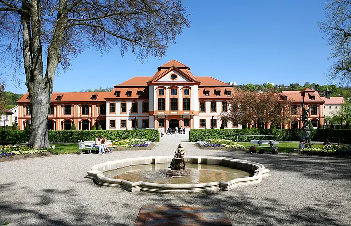 In der Mitte des Bildes befindet sich die Sommerresidenz des Eichstätter Hofgartens. Das mehrstöckige Residenzgebäude erstreckt sich quer über das ganze Bild. Der Anstrich des Gebäudes ist weiß und bildet somit einen Kontrast zu den orangen umrandeten Fenstern und Türen sowie den mit roten Ziegeln bedeckten Dach. Davor liegt ein Brunnen mit einer wasserspeienden Skulptur. Der Brunnen wird von einem Kiesweg, der auf das Residenzgebäude zuführt, umrandet. Rechts und links sind Grünflächen, die mit Bäumen, Hecken und Blumen bepflanzt sind.
