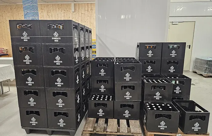 Schwarze Getränkekisten mit Flaschen der Marke Schwarzer Bräu gestapelt auf Paletten in einem Lagerraum.