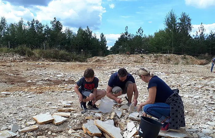 Eine Familie kniet im Steinbruch und sucht mit Hammer und Meißel nach Versteinerungen.