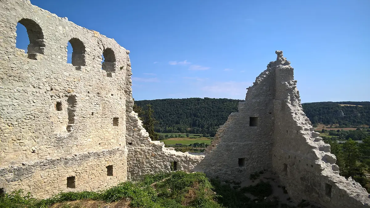 Ruine Rumburg Links steht noch eine komplette Wand mit drei Rundbögenfenstern. Rechts sind nur noch die Teile zweier Mauern an der Ecke zu sehen. Im Hintergrund hat man einen schönen Blick ins Tal. Der Himmel ist wolkenlos.