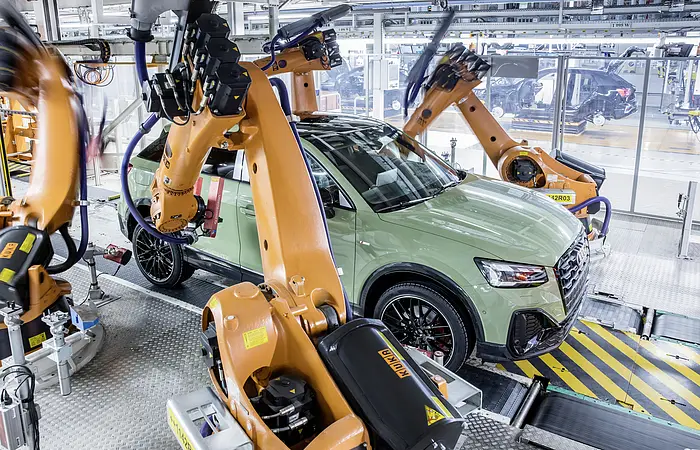 Eine A3 Limousine in hellem pastellgrün ist auf der Montage Linie zusehen. Die Roboterarme arbeiten gerade an dem Fahrzeug.