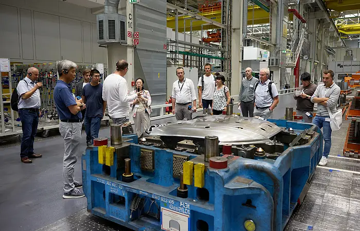 Eine Besuchergruppe steht in der Produktion vor einer Maschine und hört gebannt den interessanten Ausführungen zu.