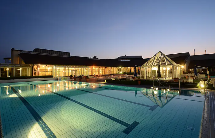 Die Therme und das Außenbecken hell erleuchtet in der Nacht.