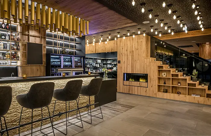 Die Bar ist in goldbraunen Tönen eingerichtet. Die Bar links mit den vollen Regalen und rechts eine treppenartiges Möbel.
