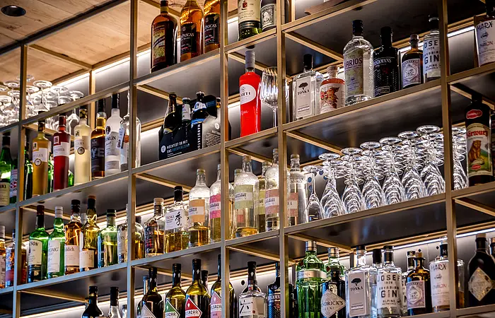 Wein- und Cocktailgläser, daneben zahlreiche Wein- und Schnapsflaschen in einem offenem Regal zu bestaunen.