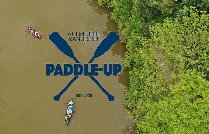 Luftaufnahme von zwei Kanus auf einem Fluss neben grünem Ufer mit Logo „Altmuehl Kanurent Paddle-Up“ und zwei gekreuzten Paddeln.