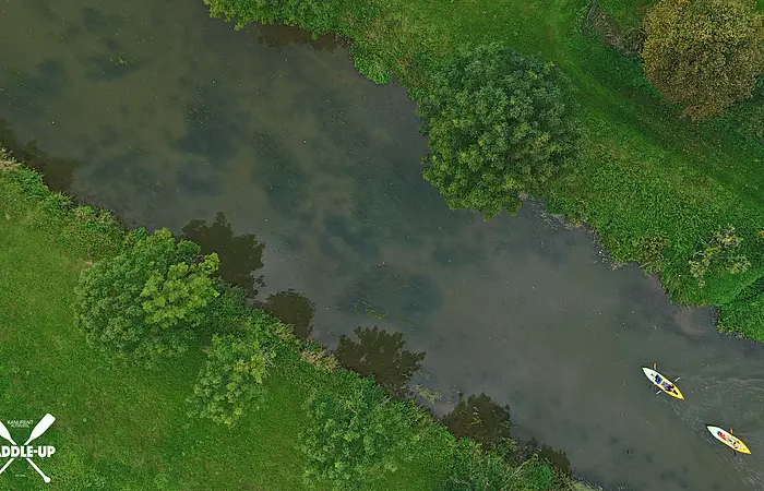 Luftaufnahme von zwei Kajakfahrern auf einem Fluss mit grünem Ufer und Bäumen.