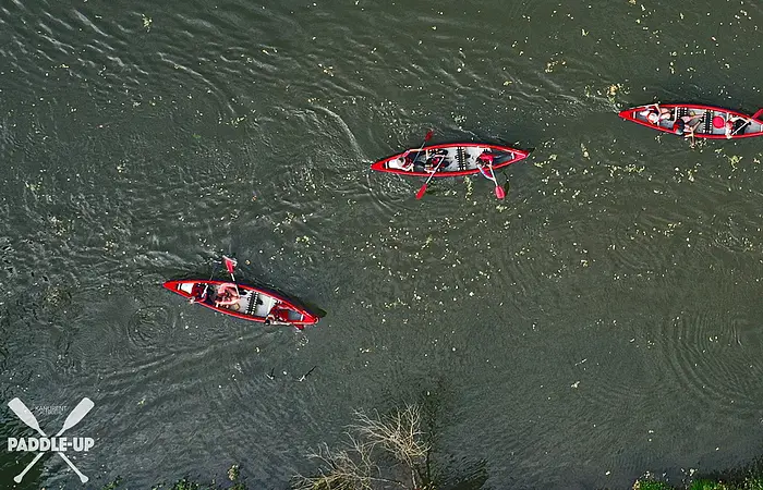 Drei rote Kanus mit jeweils zwei Personen paddeln auf einem Fluss, Luftaufnahme von oben.