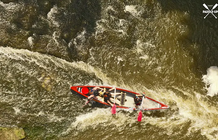 Drei Personen paddeln in einem roten Kanu auf einem fließenden, schäumenden Fluss von oben gesehen.