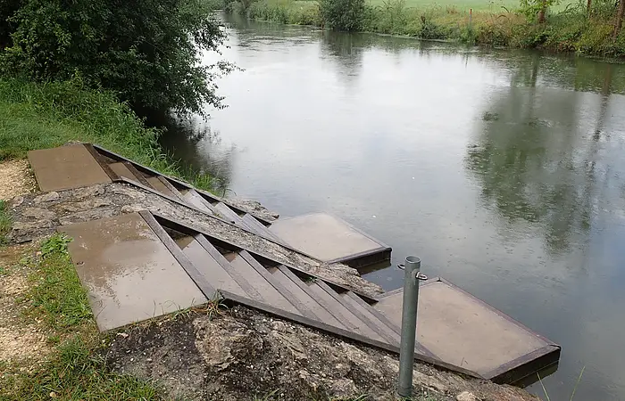 Ufer mit Treppe und Plattformen am ruhigen Fluss bei bewölktem Himmel und Regen.