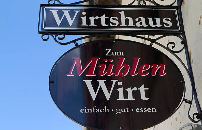 Das Wirtshausschild groß fotografiert. Man erkennt nur noch den blauen Himmel und die Hausfassade.