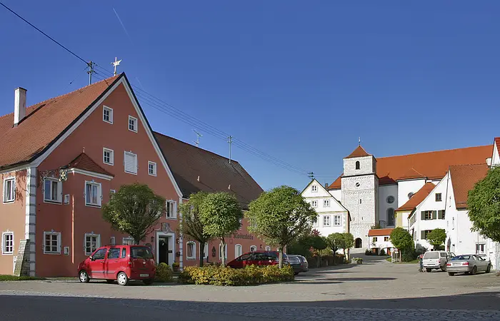 Blick auf die Klosterkirche Heilig Kreuz in Bergen bei Neuburg a. d. Donau. Im Vordergrund ist das Hotel Klosterbräu mit roter Außenfassade zu sehen.