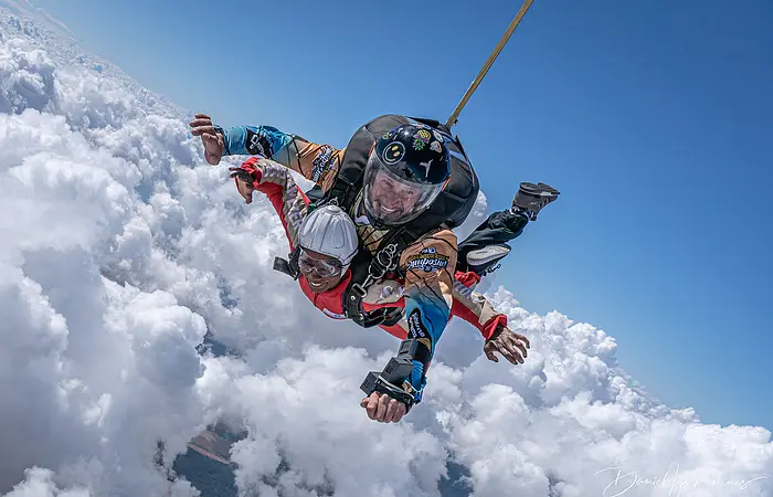 Zwei Tandemspringer bei blauem Himmel oberhalb der Wolkendecke.
