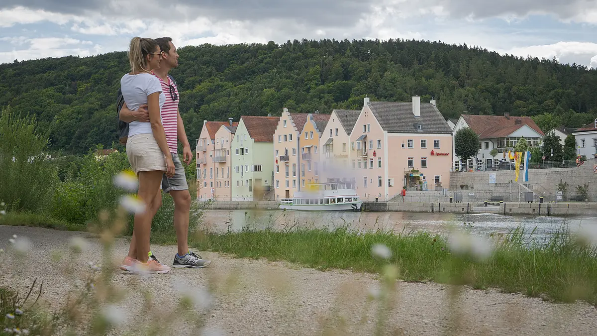 Pärchen am Main-Donau-Kanal bei Riedenburg Ein Pärchen in sommerlicher Kleidung steht am Main-Donau-Kanal und halten sich im Arm. Sie schauen aufs Flussufer gegenüber, dort ist die Riedenburger Promenade zu sehen. Dahinter ragen die Hänge mit ihrem dunkelgrünen Kleid auf.