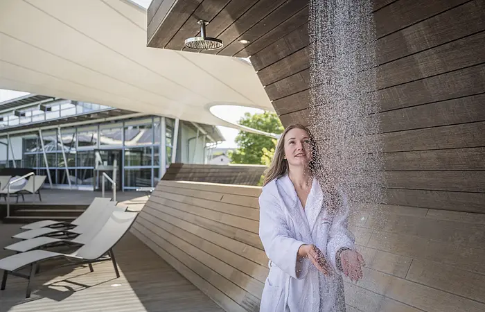 Frau im Bademantel hält ihre Hände unter den Wasserfall