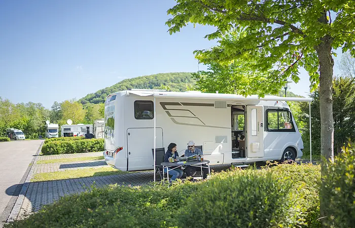 Pärchen sitzt vor dem Wohnmobil an einem Tisch und liest in der NPA-Zeitung