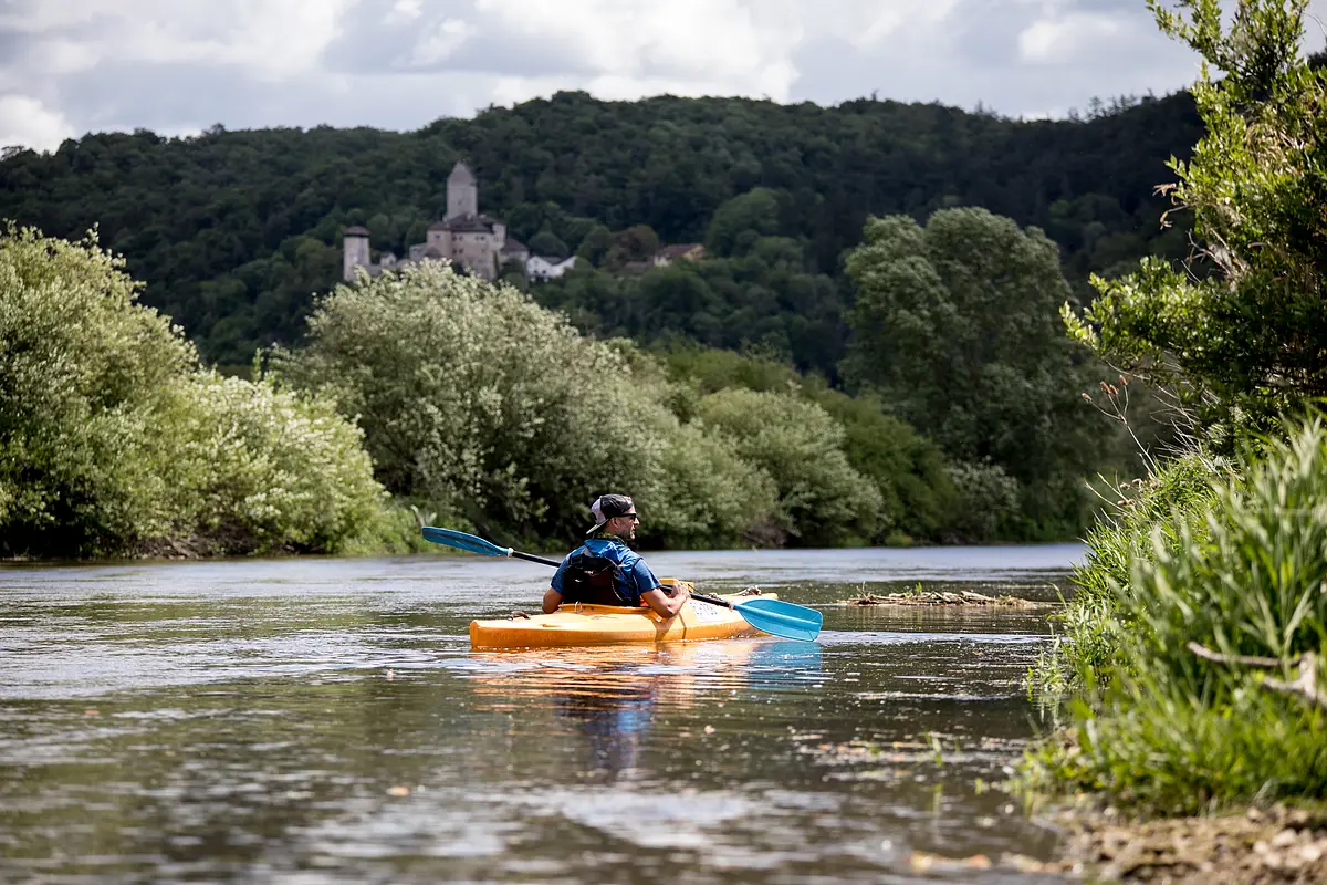Bootwanderer auf der Altmühl bei Kipfenberg Ein Kanufahrer in einem orangenen Kanu paddelt auf der Altmühl. Über ihm trohnt die Burg Kipfenberg inmitten des Waldes am Hang.