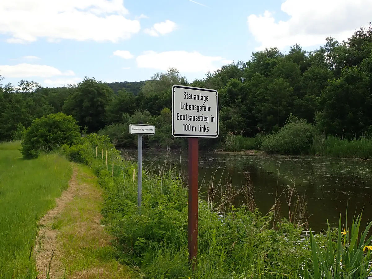 Warnschild an der Altmühl Ein Schild mit weißen Hintergrund und schwarzer Schrift weißt die Bootsfahrer darauf hin, dass in 100m eine Stauanlage kommt und man das Boot umtragen muss.