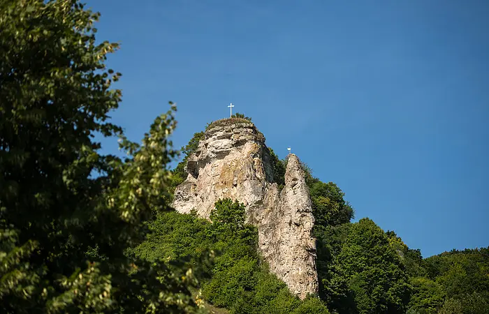 Blick von unten auf den Flügelsberg, auf dessen Spitze ein Kreuz steht. Der Berg ist eingebettet in sattes grün der Wälder ringsherum.