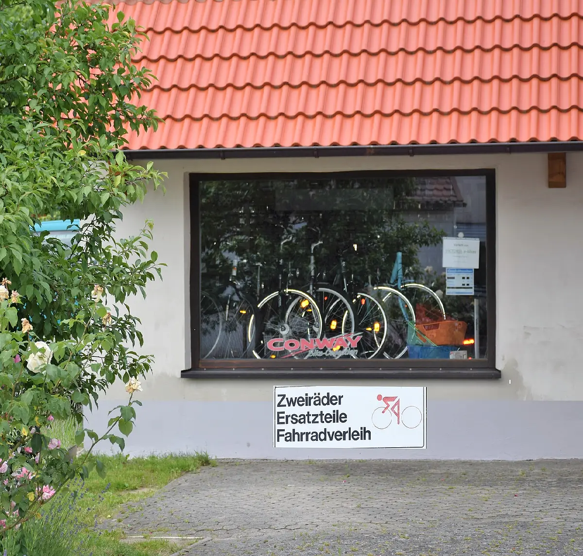 Fahrradverleih Rudolf Krüger Ein großes Schaufesnter in welchem Fahrräder stehen. Das Schaufenster gehört zu einem Haus mit weißer Fassade und rotem Ziegeldach.