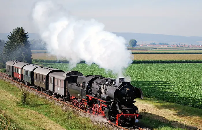 Eine Dampflokomotive mit Waggons fährt rauchend durch das Ries