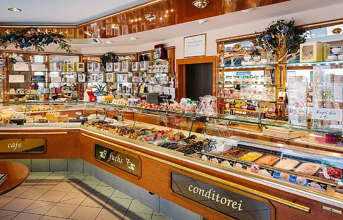 Die Theke mit Vielzahl an Produkten wie Kuchen/Torten/Pralinen und Gebäck dargestellt in dem dekorierten Eingangsraum