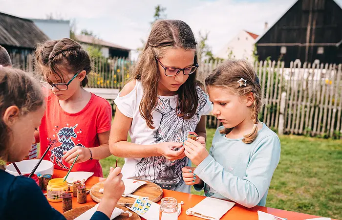 Vier Mädchen stehen an einem Biertisch im Garten des Jura-Bauernhof-Museums und basteln gemeinsam beim museumpädagischen Programm "ganz schön beeinDRUCKend".