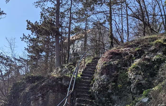 Eine Holztreppe mit Geländer schängelt sich den Berg hoch. Links geht es tief hinab.