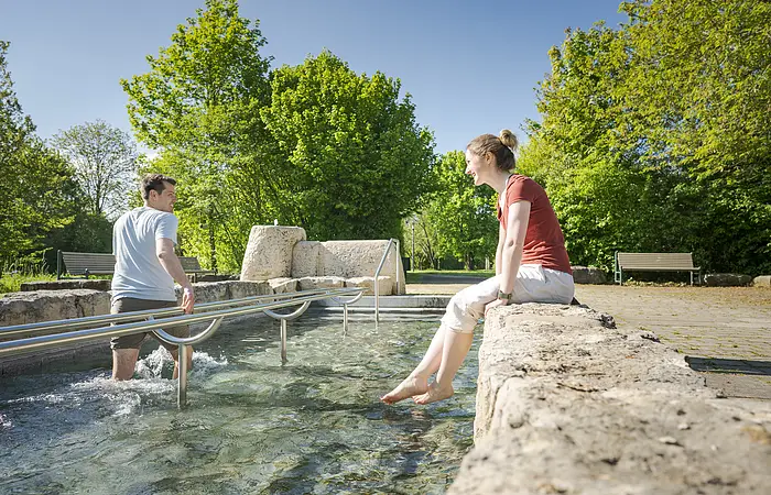 Pärchen beim Wassertreten im Kurpark. Frau schaut zu und Mann tritt Wasser.