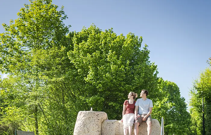 Pärchen sitzend am Wassertretbecken im Kurpark und genießen die Sonne