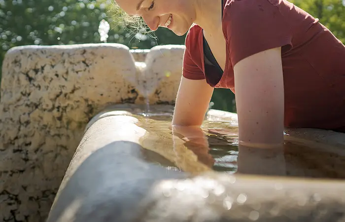 Junge Frau hält Ihre Arme ins kalte Kneippwasser und hat sichtlich Spaß dabei.