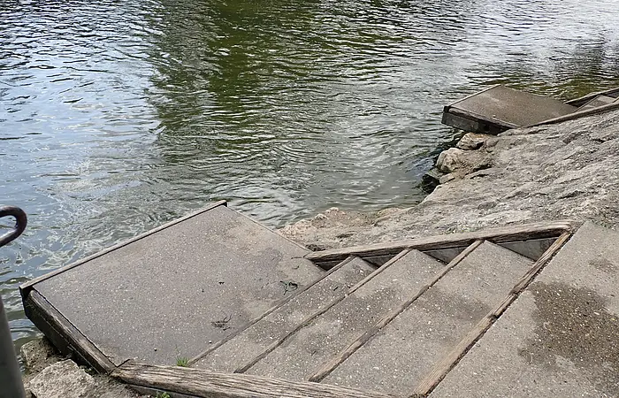 Betonstufen mit Holzgeländer führen von einem Ufer zum Wasser eines Flusses oder Sees.