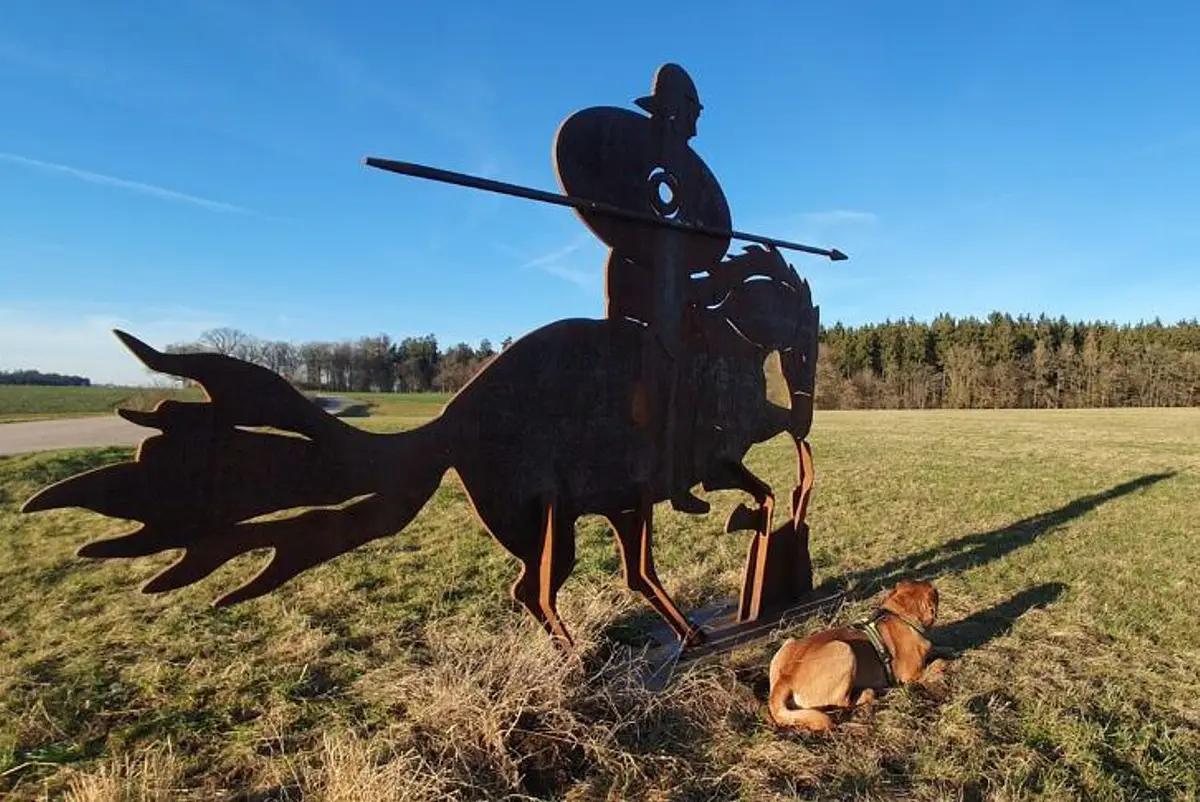 Metallrömer in Burgsalach Eine Römerfigur auf einem Pferd. Pferd und Reiter wurden aus einer Metallplatte ausgeschnitten. Die Skulptur steht auf einer grünen Wiese.