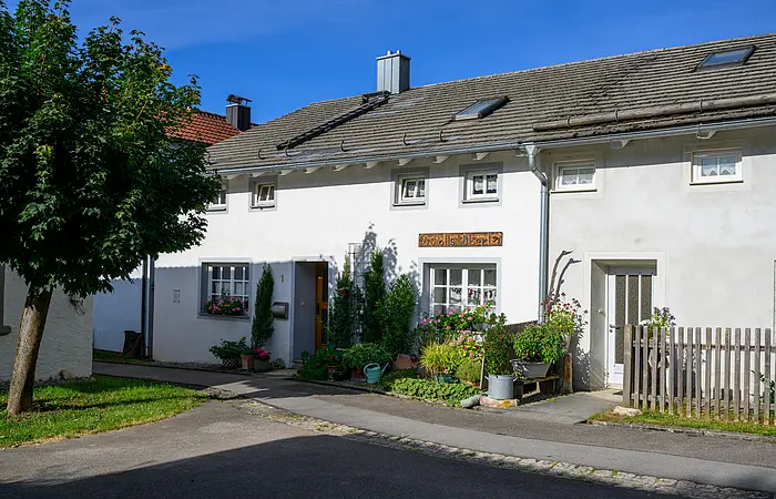 Ein Jurahaus in Suffersheim, das Wollstüberl. vor dem Haus befinden sich einige Stäucher, Die Tür und die Fenster sind mit einem hellgrauen Farbanstrich abgesetzt