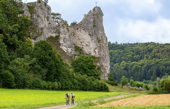 Zwei Rennradler fahren unterhalb des massiven Burgsteinfelsen gen Dollnstein