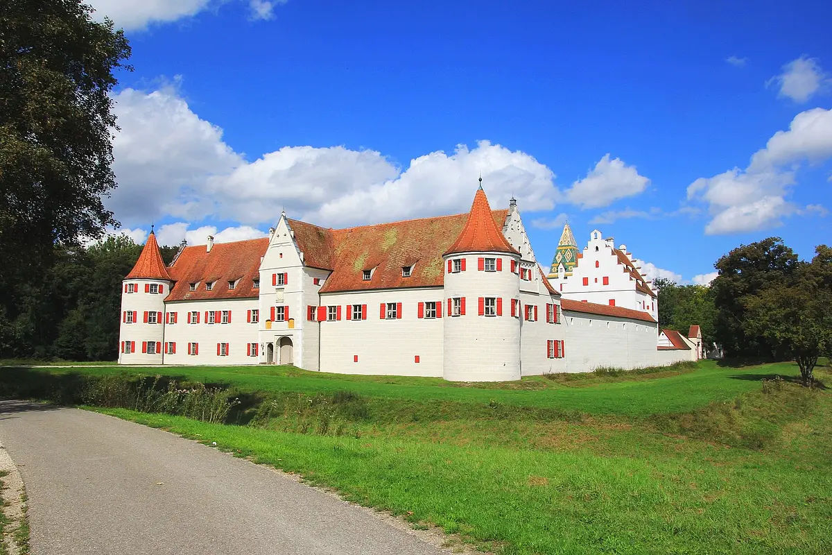 Das Schloss mit seinen roten Fensterläden und roten Dächern inmitten grüner Wiesen.