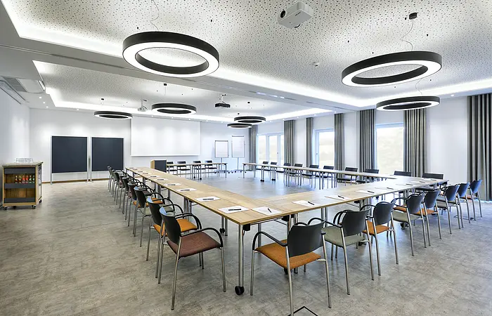 Konferenzraum mit U-förmiger Tischanordnung, Stühlen, moderner Beleuchtung und Präsentationsflächen.
