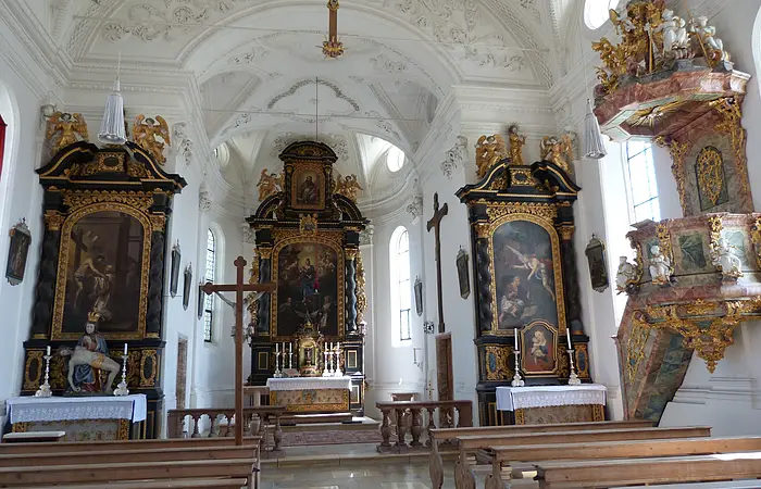 Blick in die helle, lichtdurchflutete Schlosskirche. Vorne in der Mitte der Hauptaltar, links und rechts die Seitenaltäre sowie ganz rechts im Bild die Kanzel.