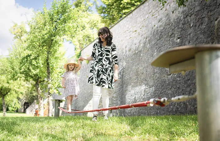 Eine Frau hilft ihrem Kind beim balancieren auf der Slackline im Stadtgraben.