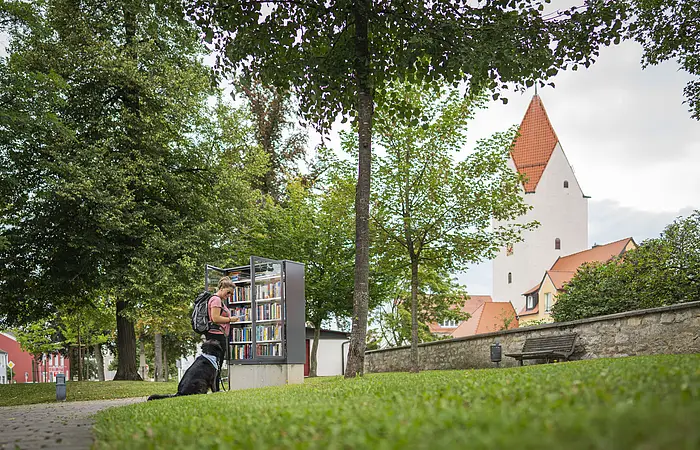 Eine Frau steht mit ihrem Hund am Bücherschrank im Stadtgraben Wemding.